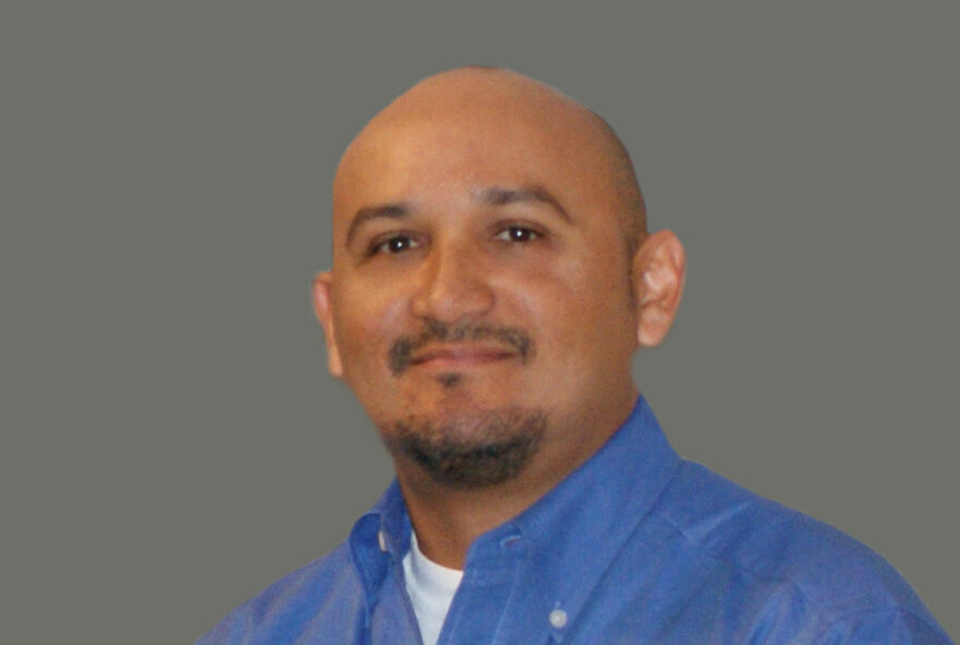 Rodriguez-Antonio smiling in a blue shirt against a gray background