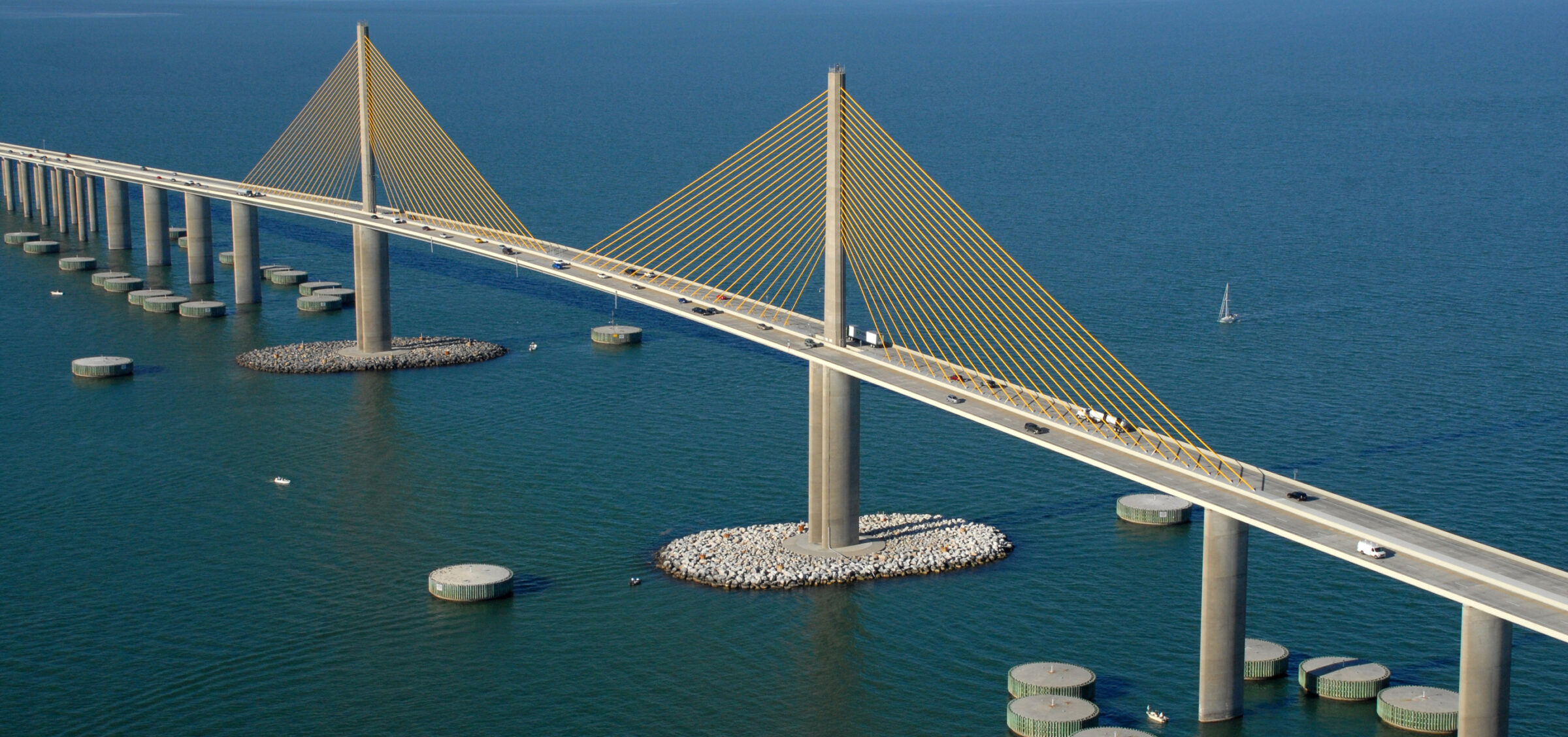 Cable-stayed bridge over blue water, with vehicles crossing; distant skyline visible