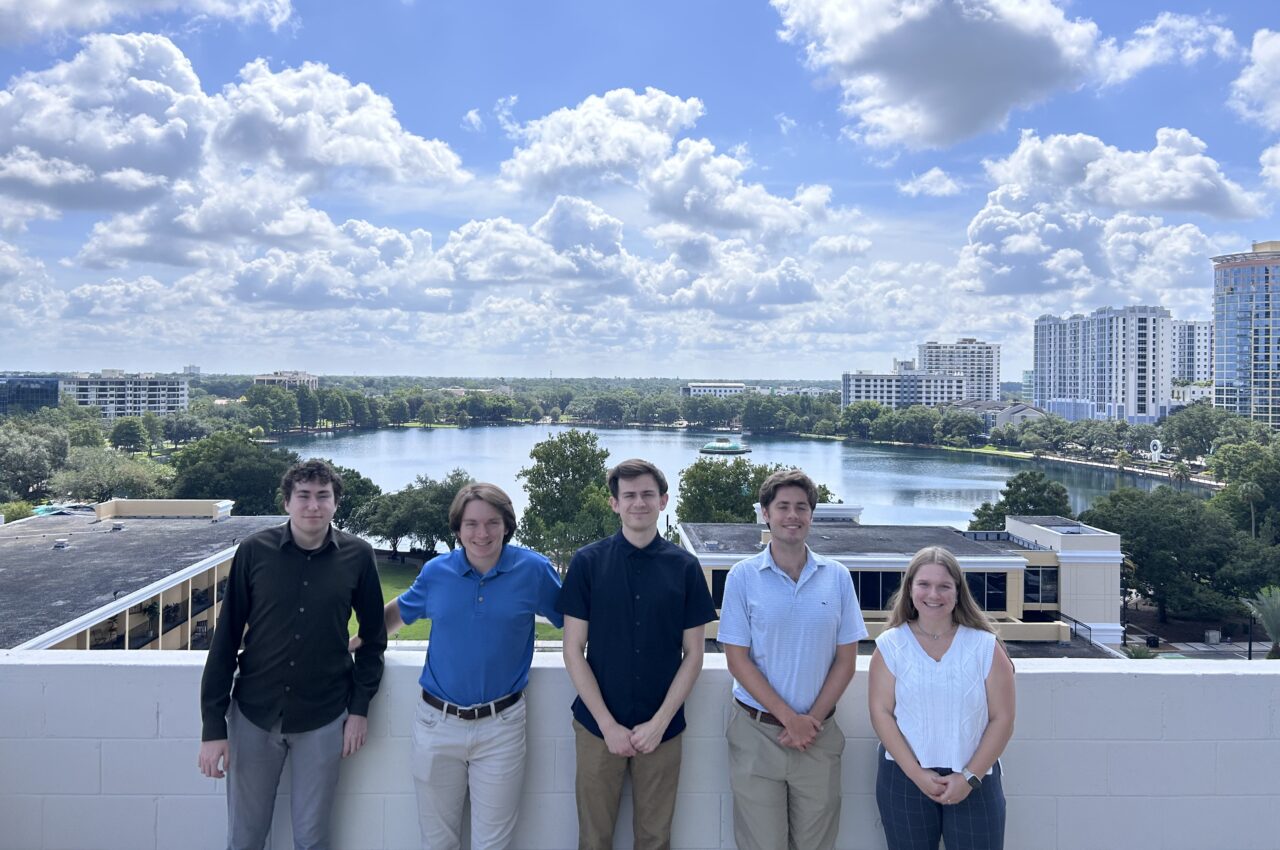 Five people smiling on a rooftop with a lake and cityscape background