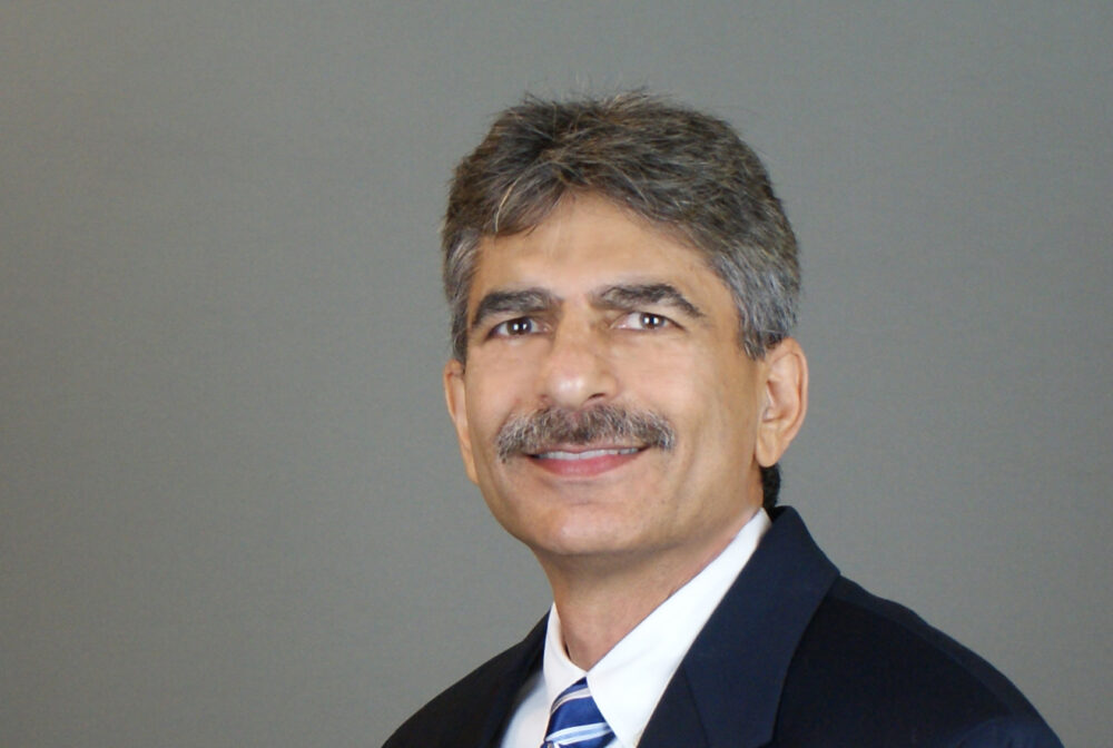 Tayebnejad smiling, wearing a blue suit and striped tie