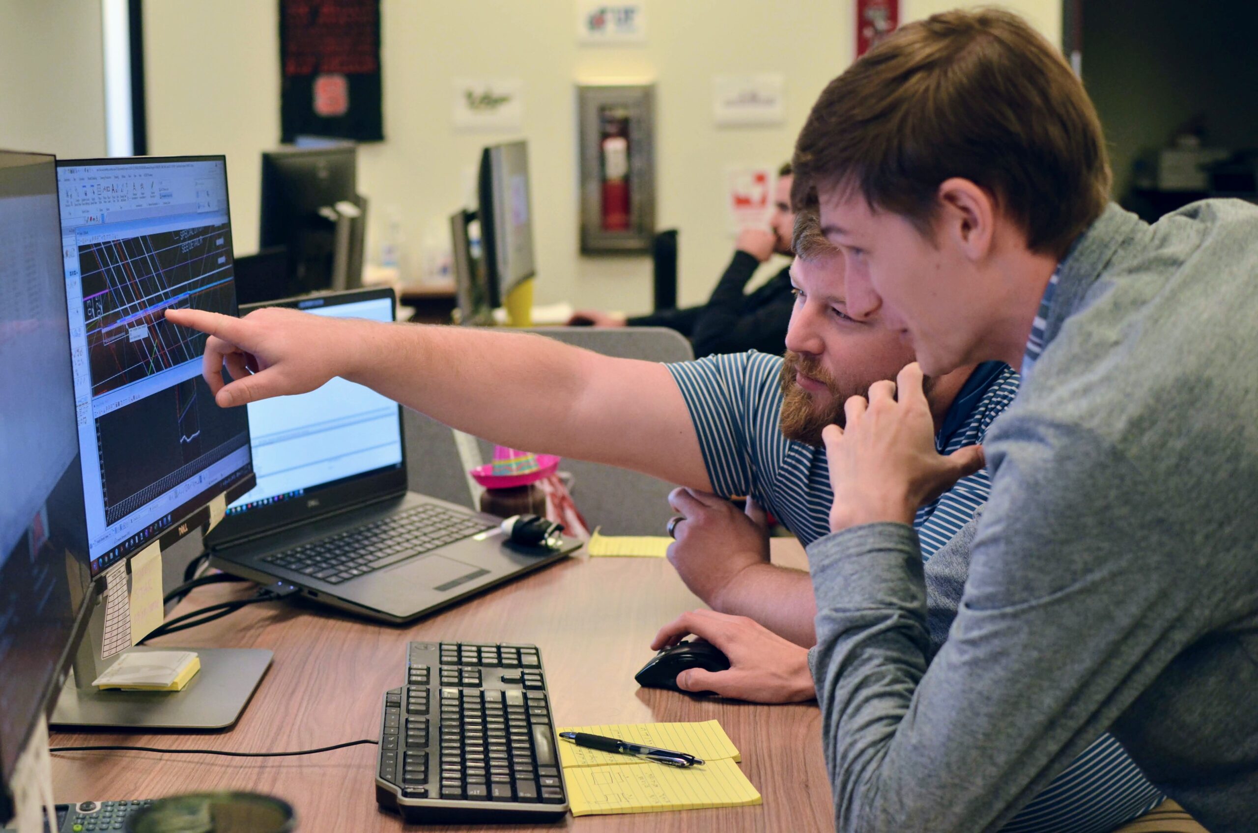 Two men collaborating at a desk, analyzing graphs displayed on a monitor