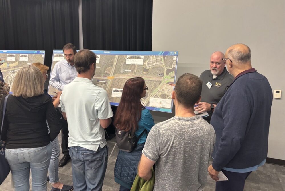 Seven people discussing road plans at a public meeting