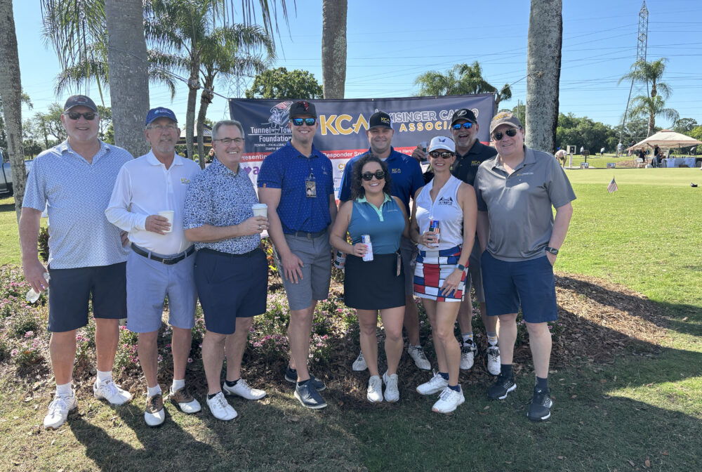Group of smiling people at a golf event with Tunnels to Towers Foundation banner