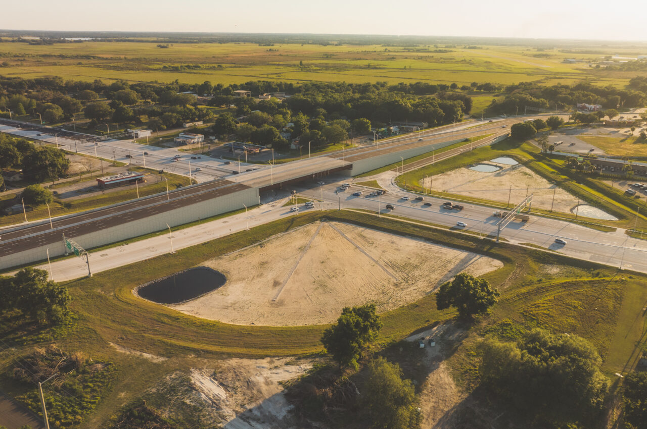 Aerial view of a highway intersection surrounded by green fields and trees under warm sunset light