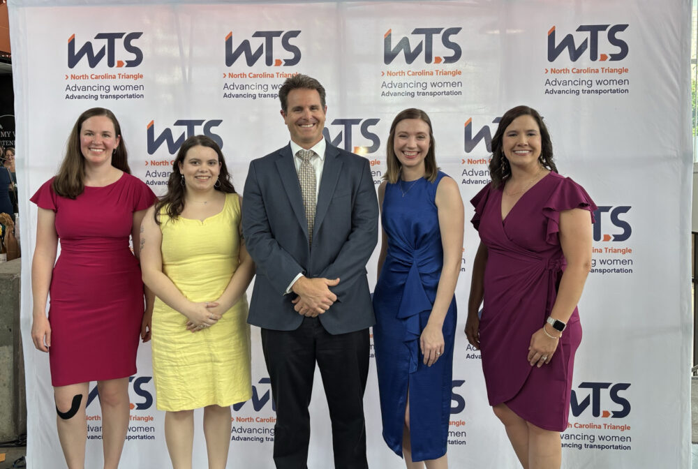 Five people smiling under neon "Raleigh" sign at WTS North Carolina Triangle event backdrop