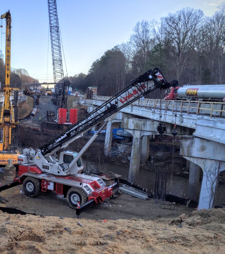 Construction site with heavy machinery and cranes working on a bridge project over a muddy area
