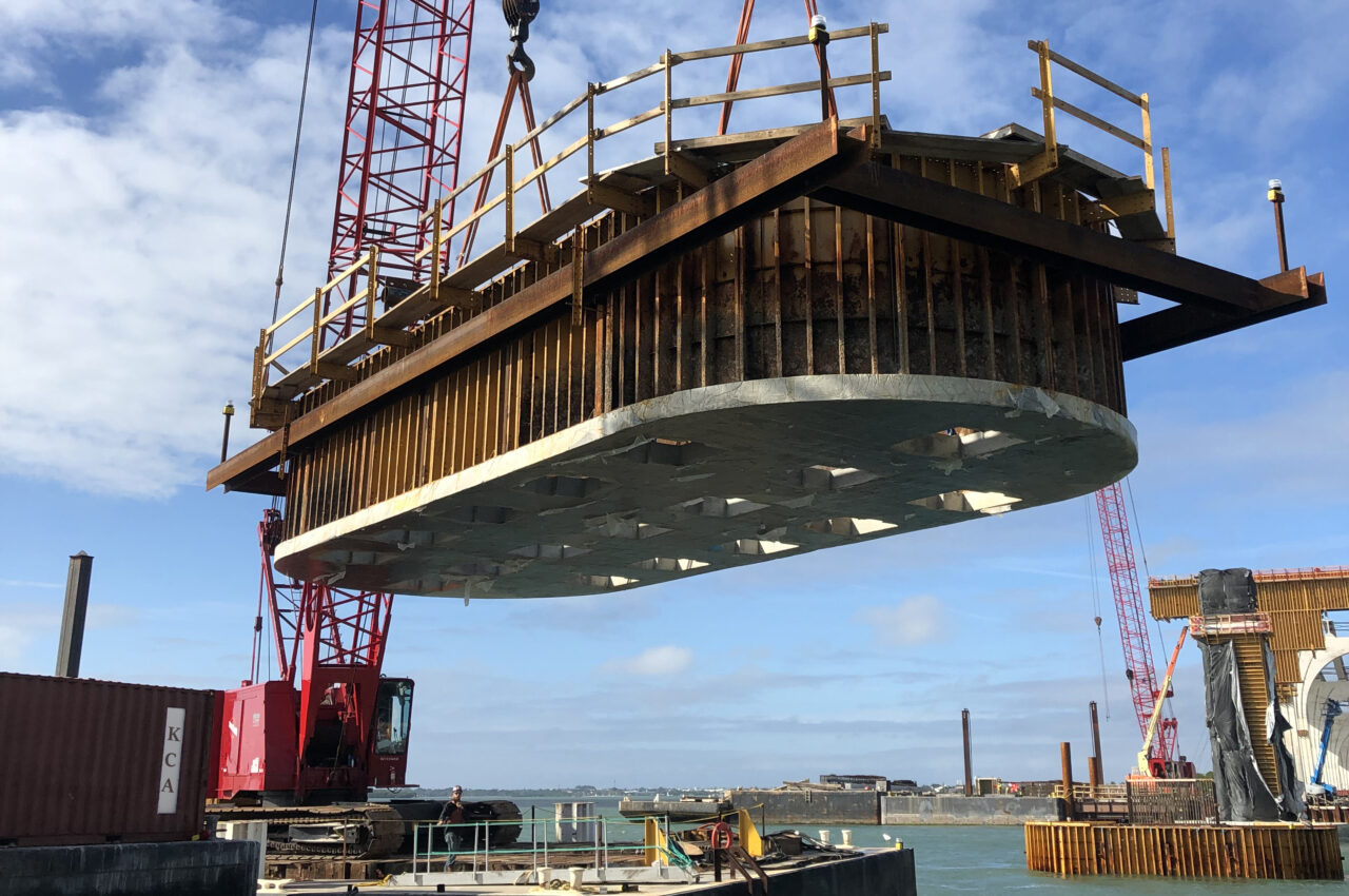 Crane lifting a large metal structure at a waterside construction site