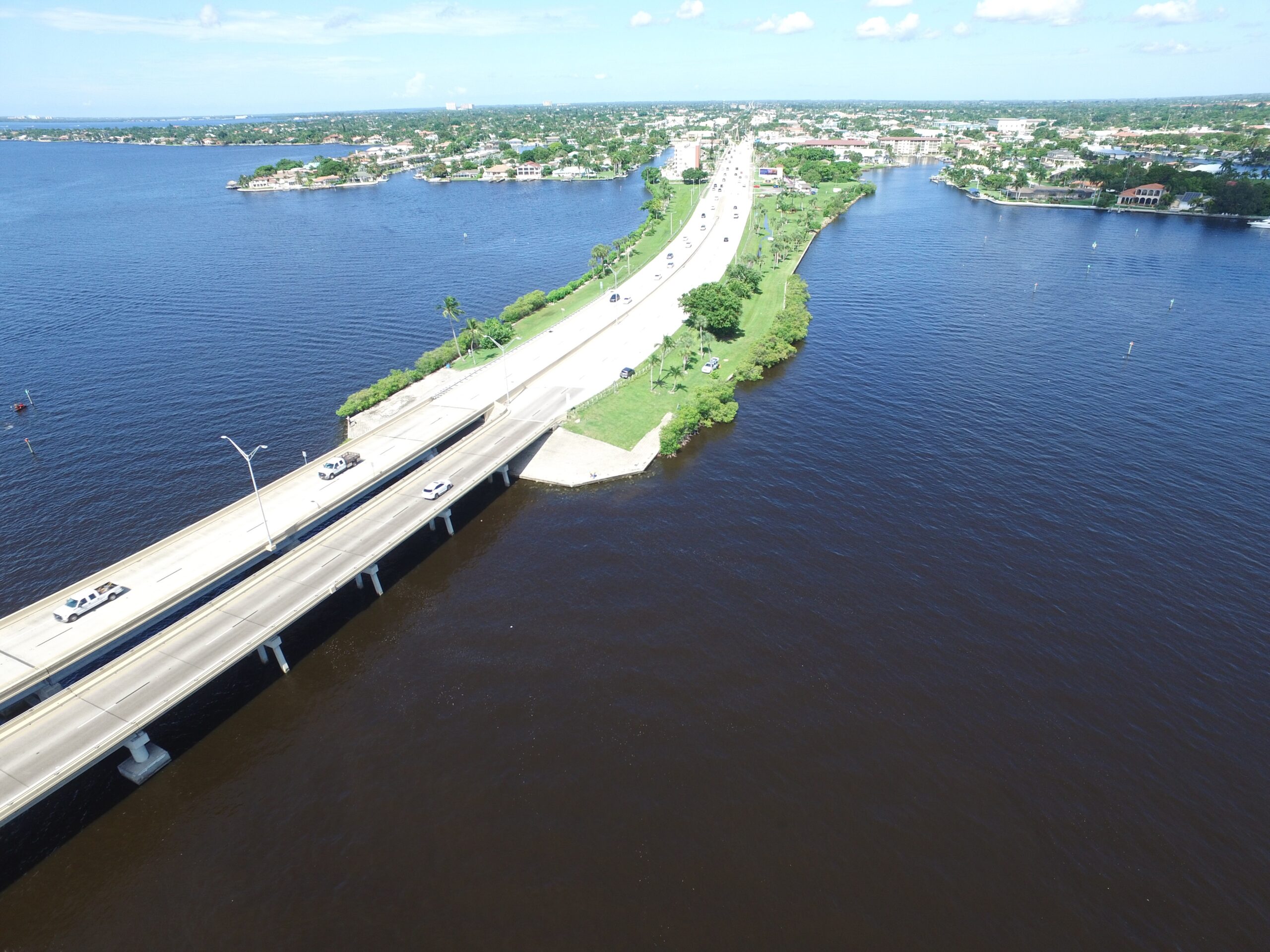 Aerial view of Cape Coral bridge over a wide river, with green shoreline and scattered houses