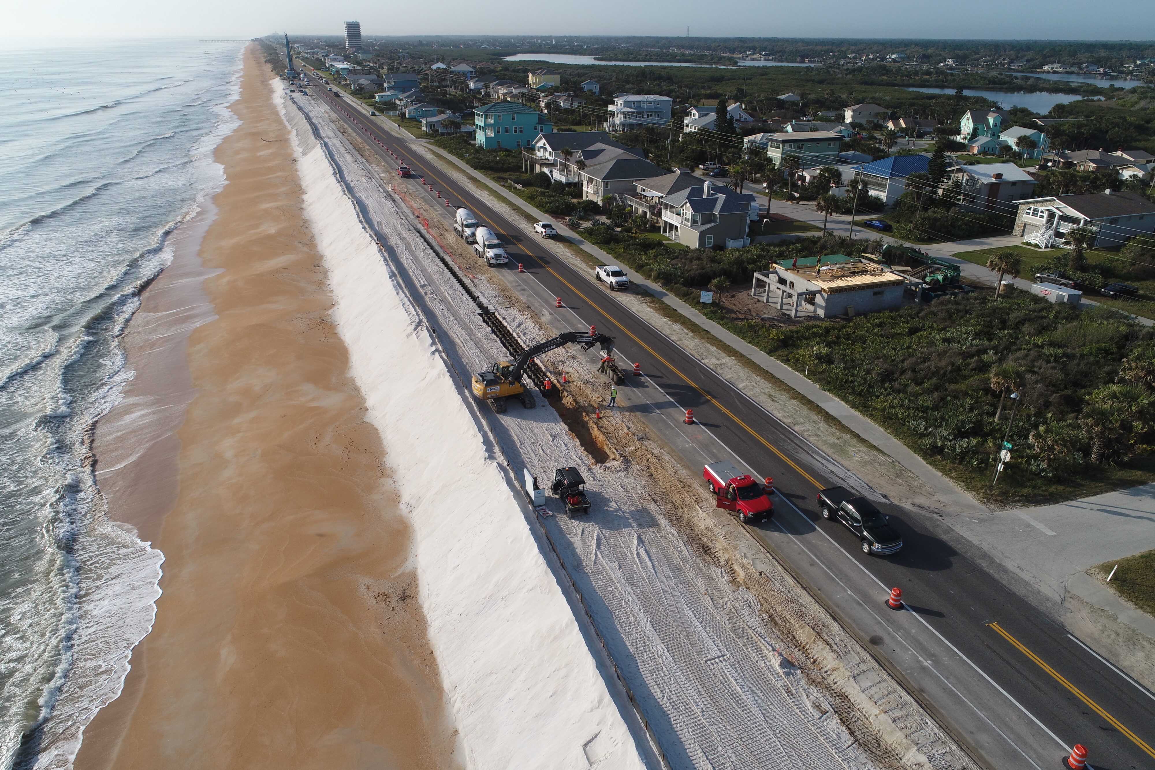 Construction work on coastal road, excavator digging beside beach, traffic diverted