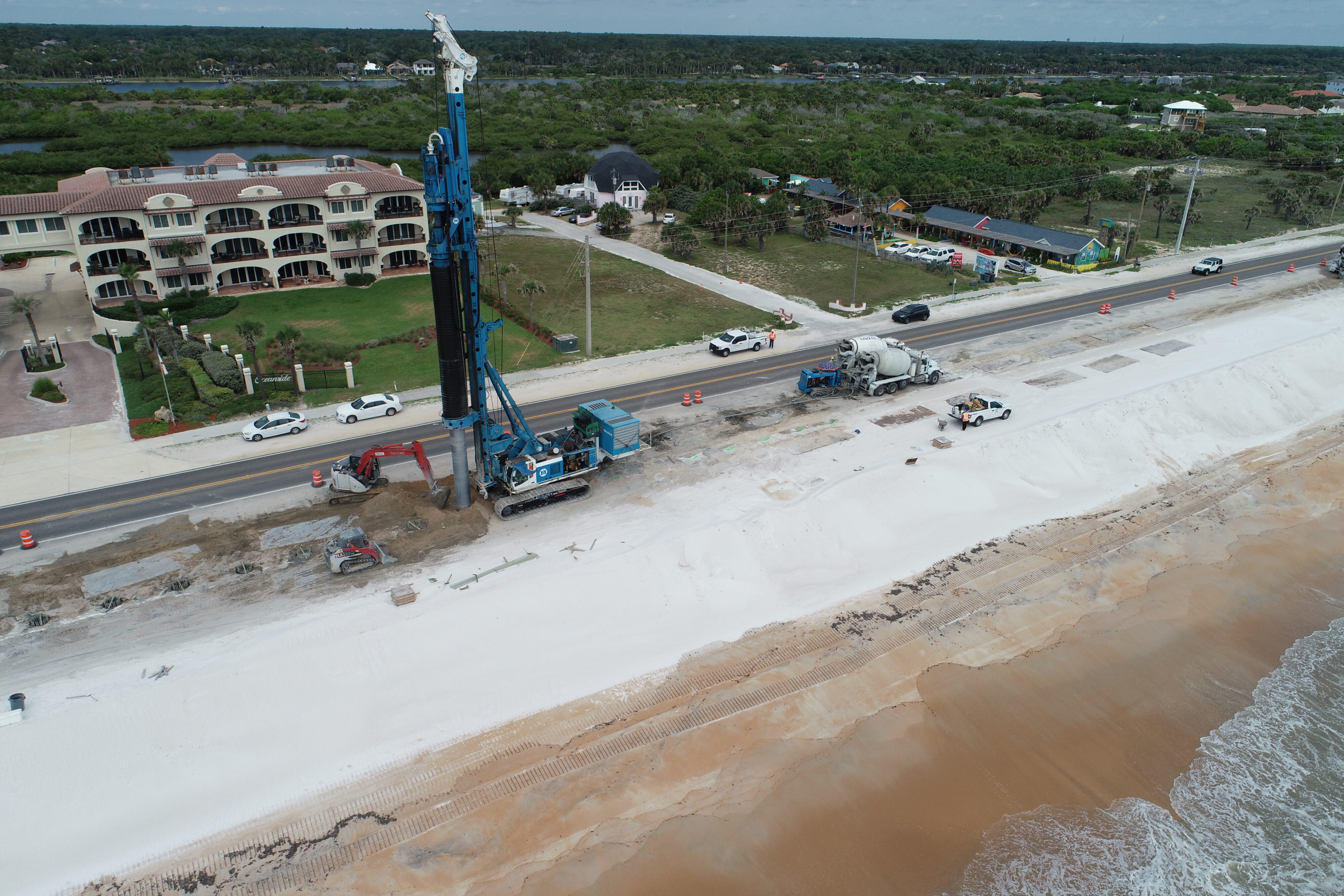 Aerial view of beach construction with heavy machinery and construction vehicles near a road