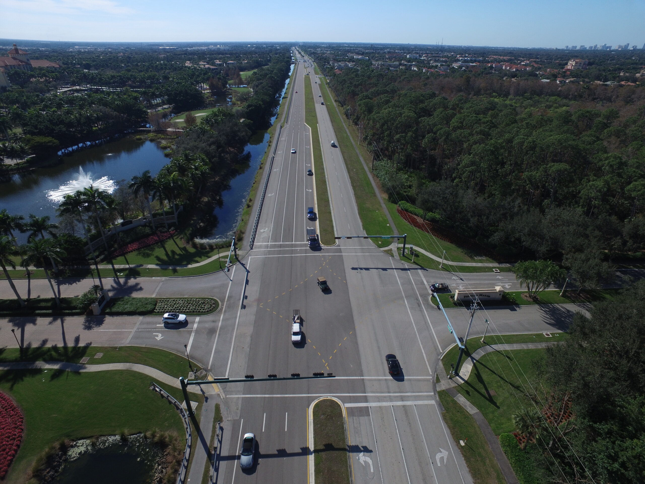 Aerial view of a multi-lane highway intersection surrounded by trees, a fountain, and distant city skyline