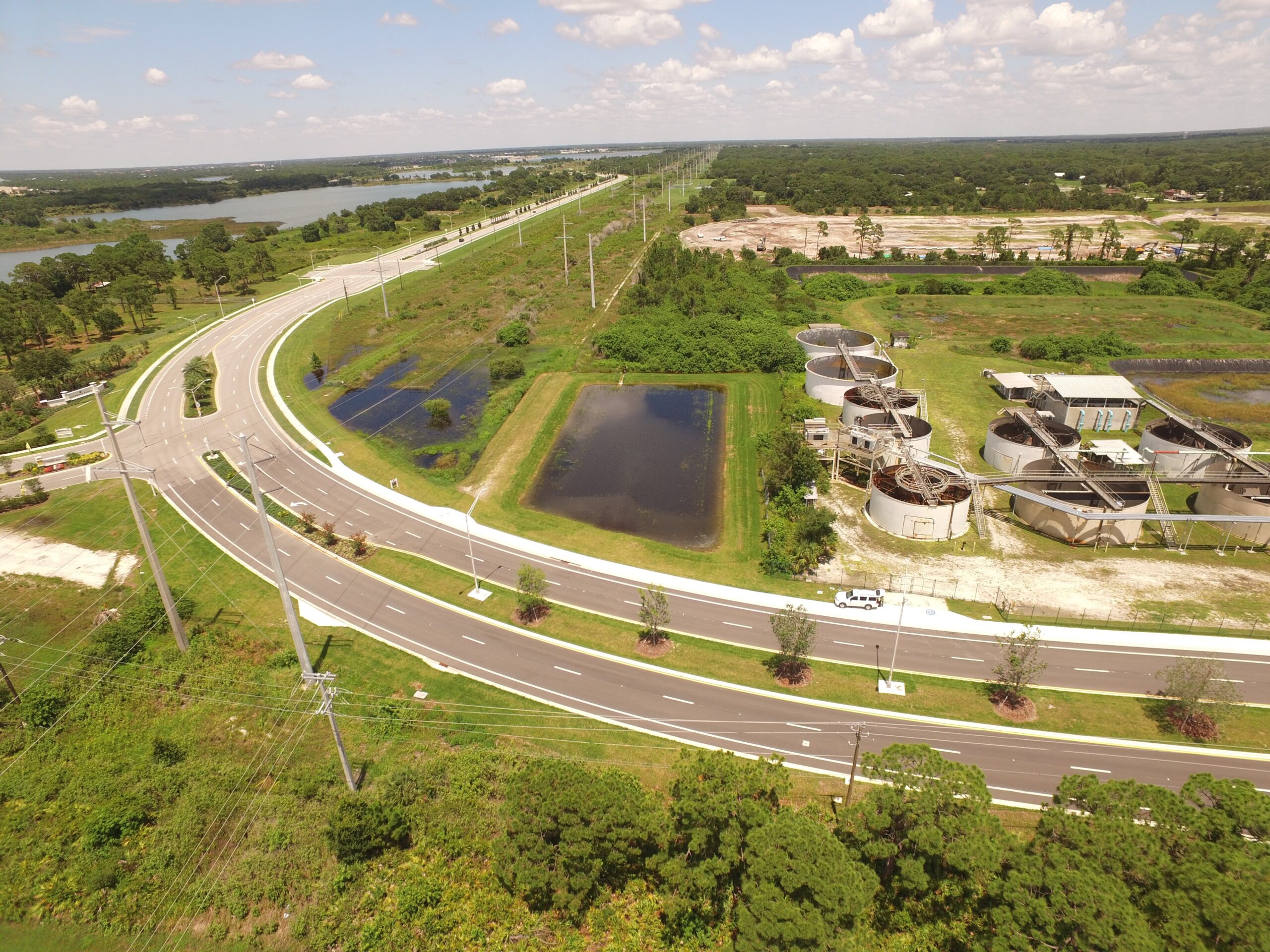 Aerial view of a wastewater treatment facility beside a curved road, surrounded by green areas and ponds