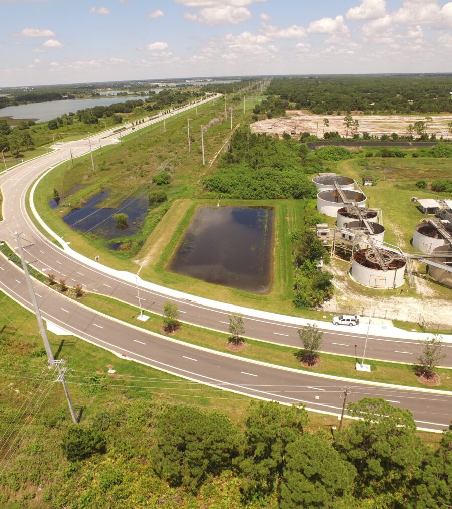 Aerial view of a wastewater treatment plant surrounded by greenery and curved roads under a partly cloudy sky