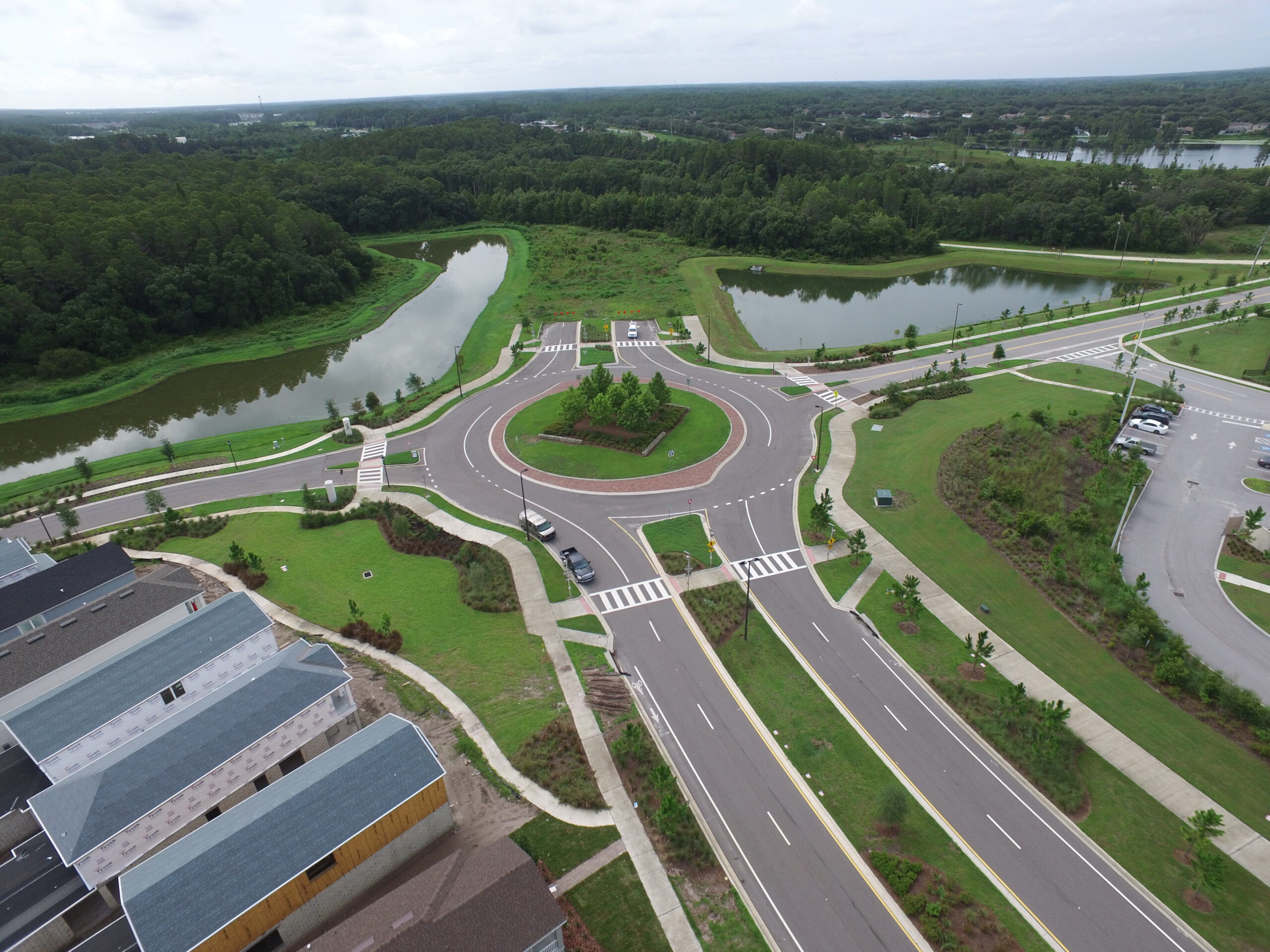 Aerial view of a roundabout surrounded by greenery and two ponds, with nearby residential buildings and parking lot