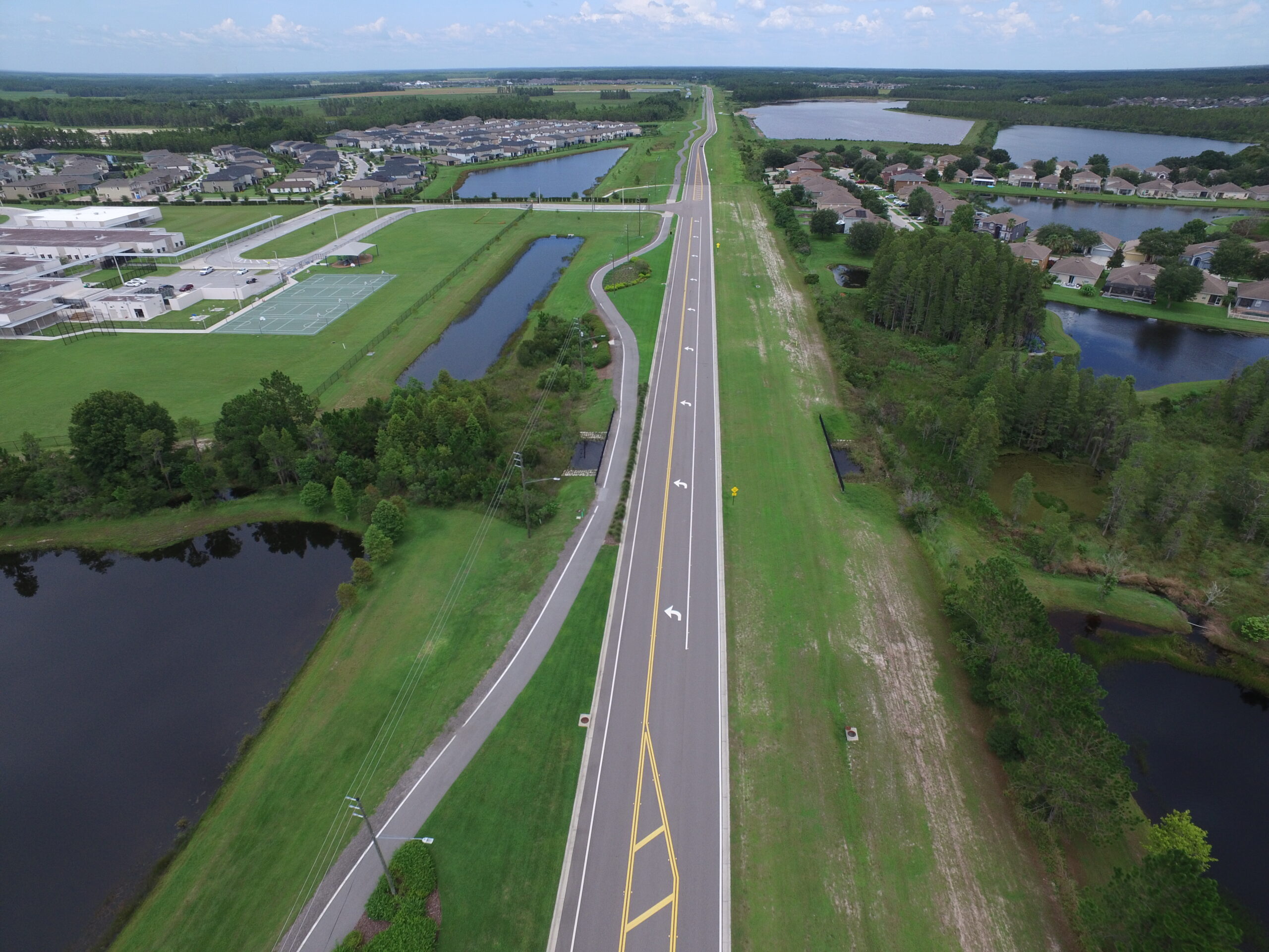 Aerial view of a suburban neighborhood with a central road, houses, ponds, and tennis courts