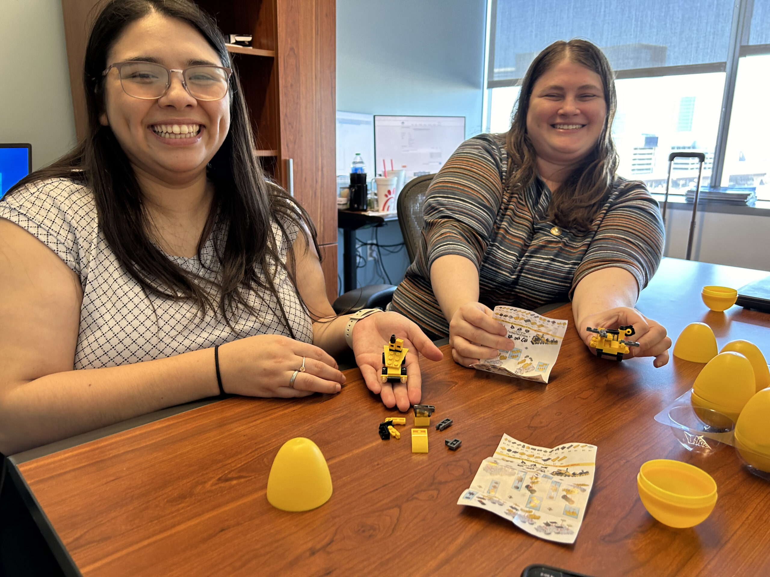 Two women smiling while assembling toy figures with instruction sheets