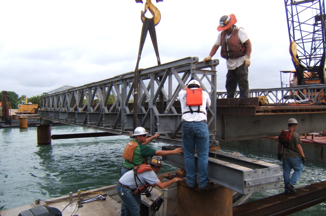 Workers assembling steel structure over water for bridge replacement project