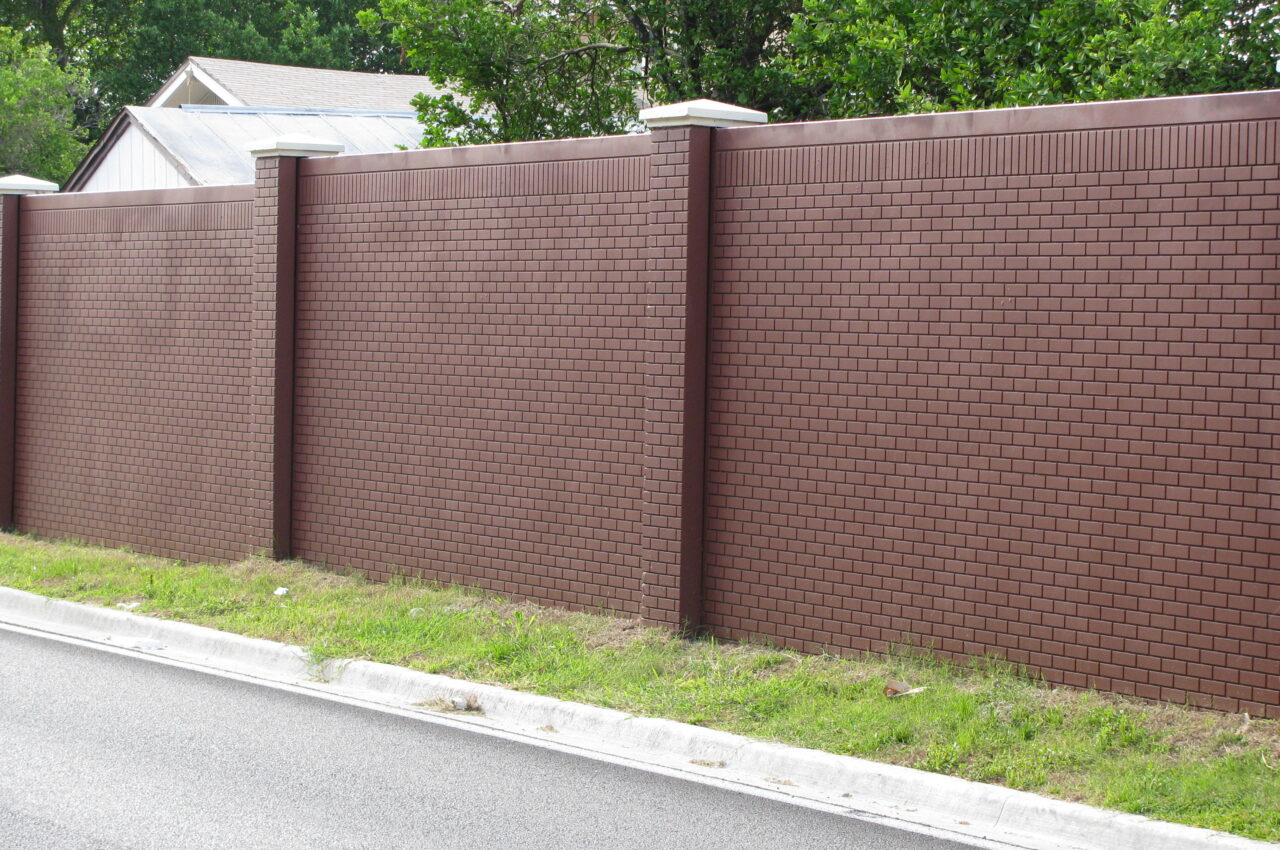 Brown brick wall along a road, greenery visible above