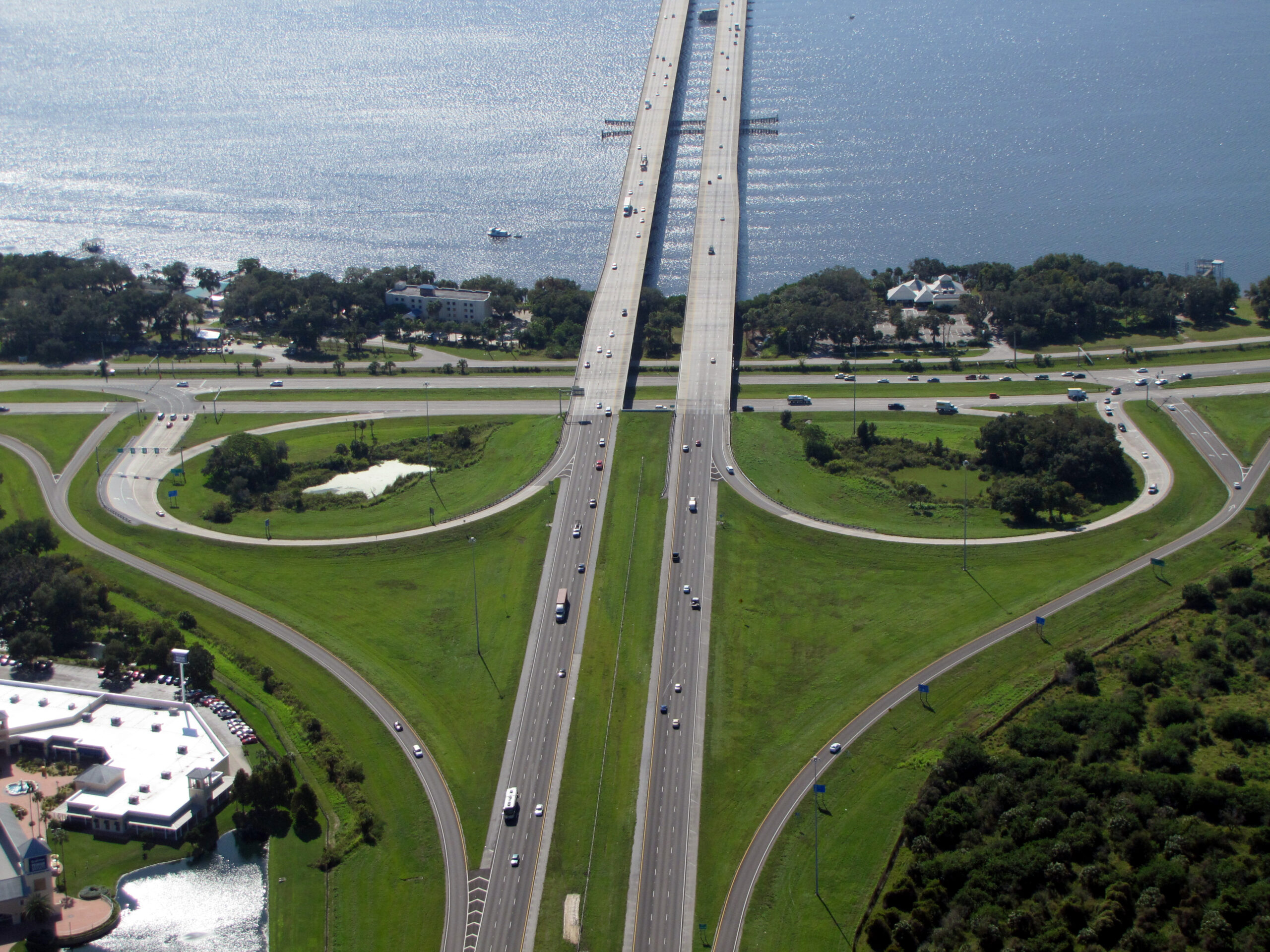 Aerial view of highway intersection near water, surrounded by greenery