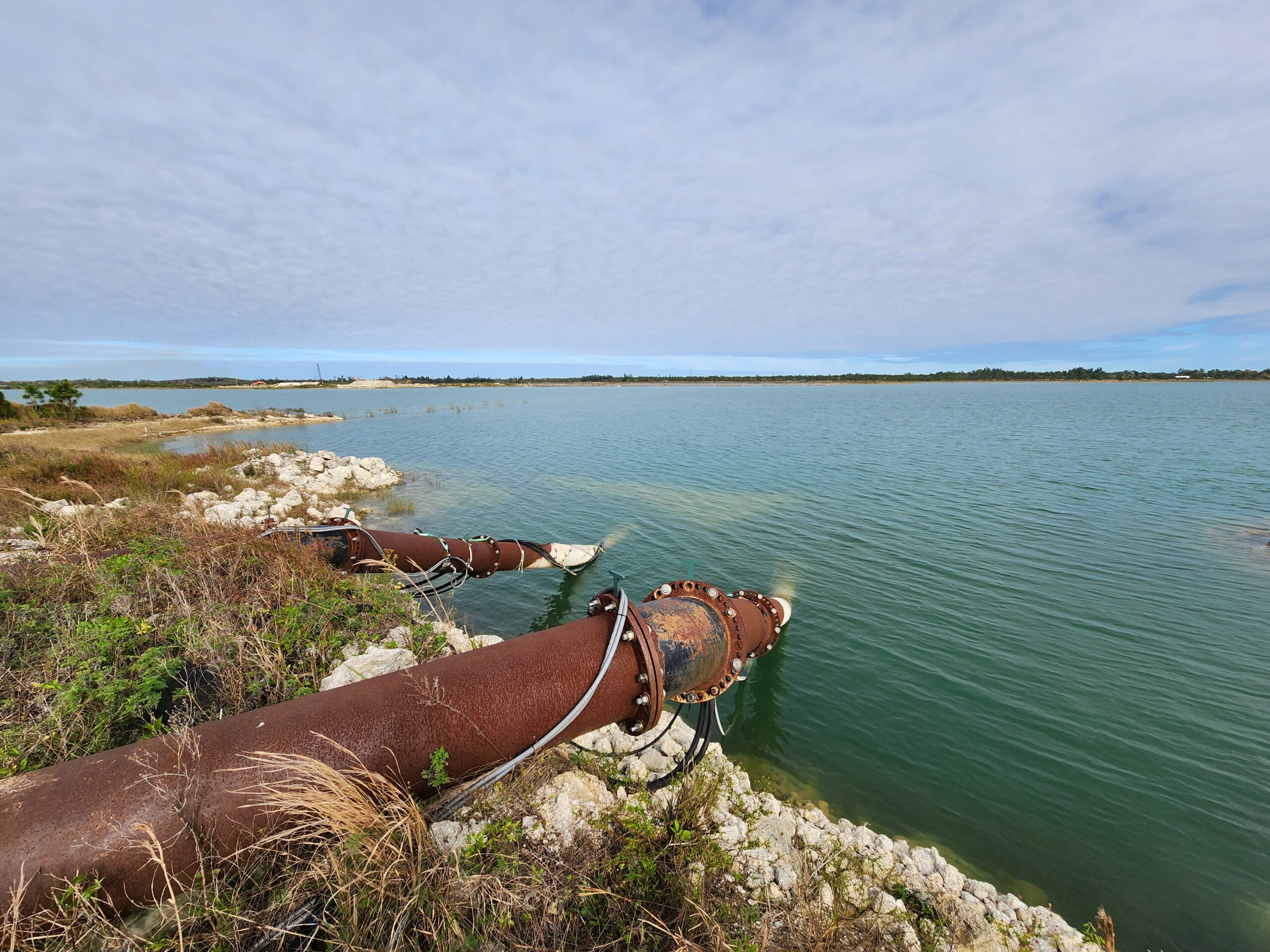 Rusty pipes discharging water into a large, calm reservoir