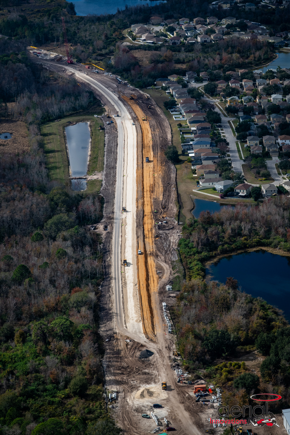 Aerial view of Ridge Road Extension construction phase, surrounded by neighborhoods, woods, and ponds; machinery on site