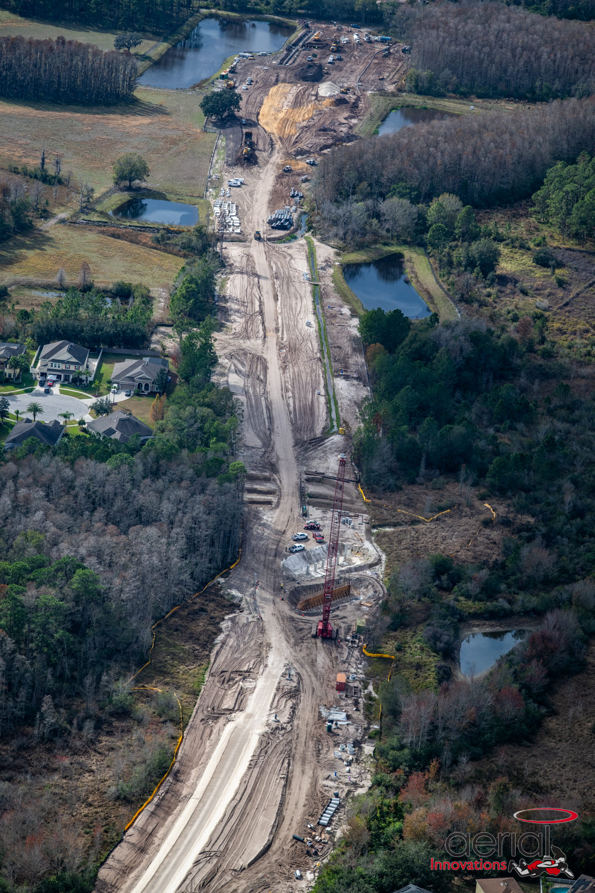 Aerial view of road construction with heavy machinery surrounded by trees and ponds