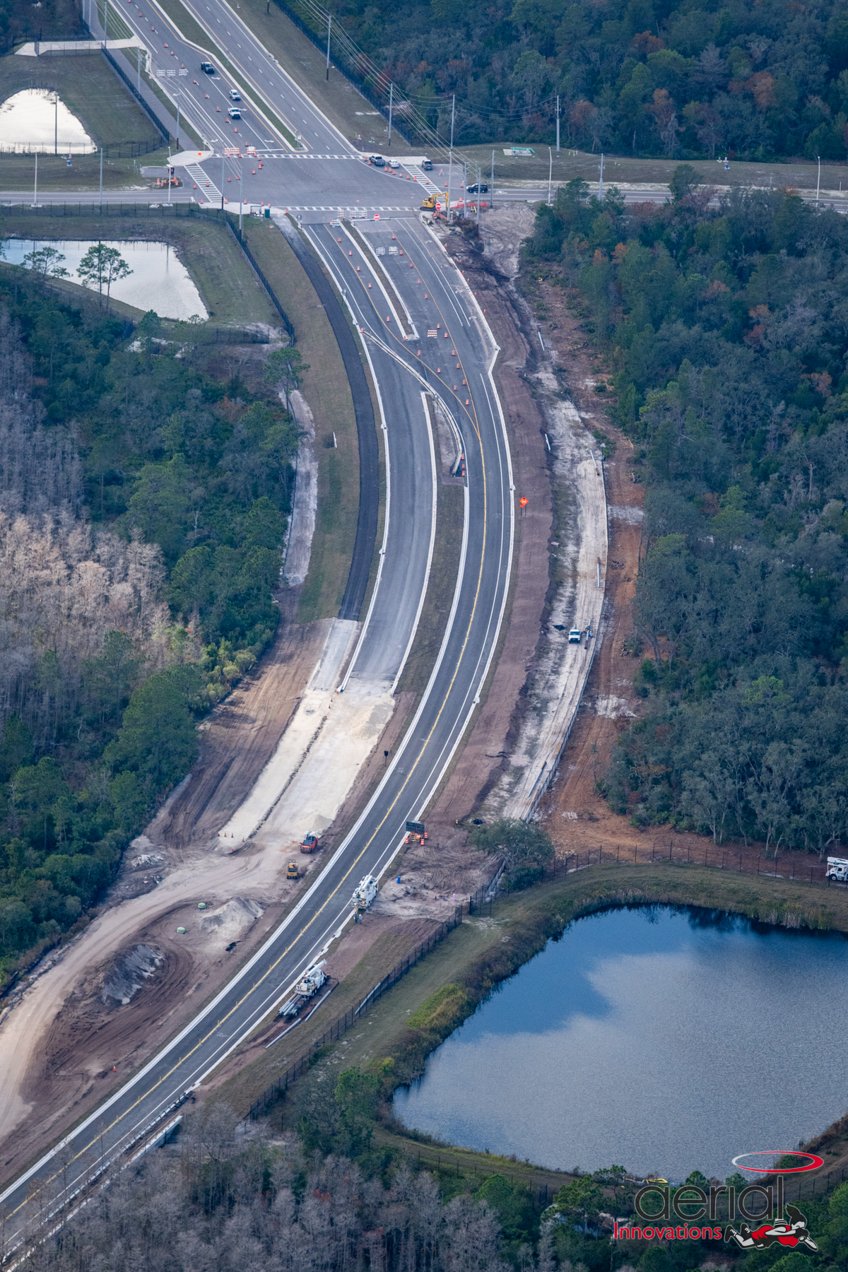 Aerial view of Ridge Road Extension construction surrounded by dense forest and ponds, showing ongoing roadwork and machinery