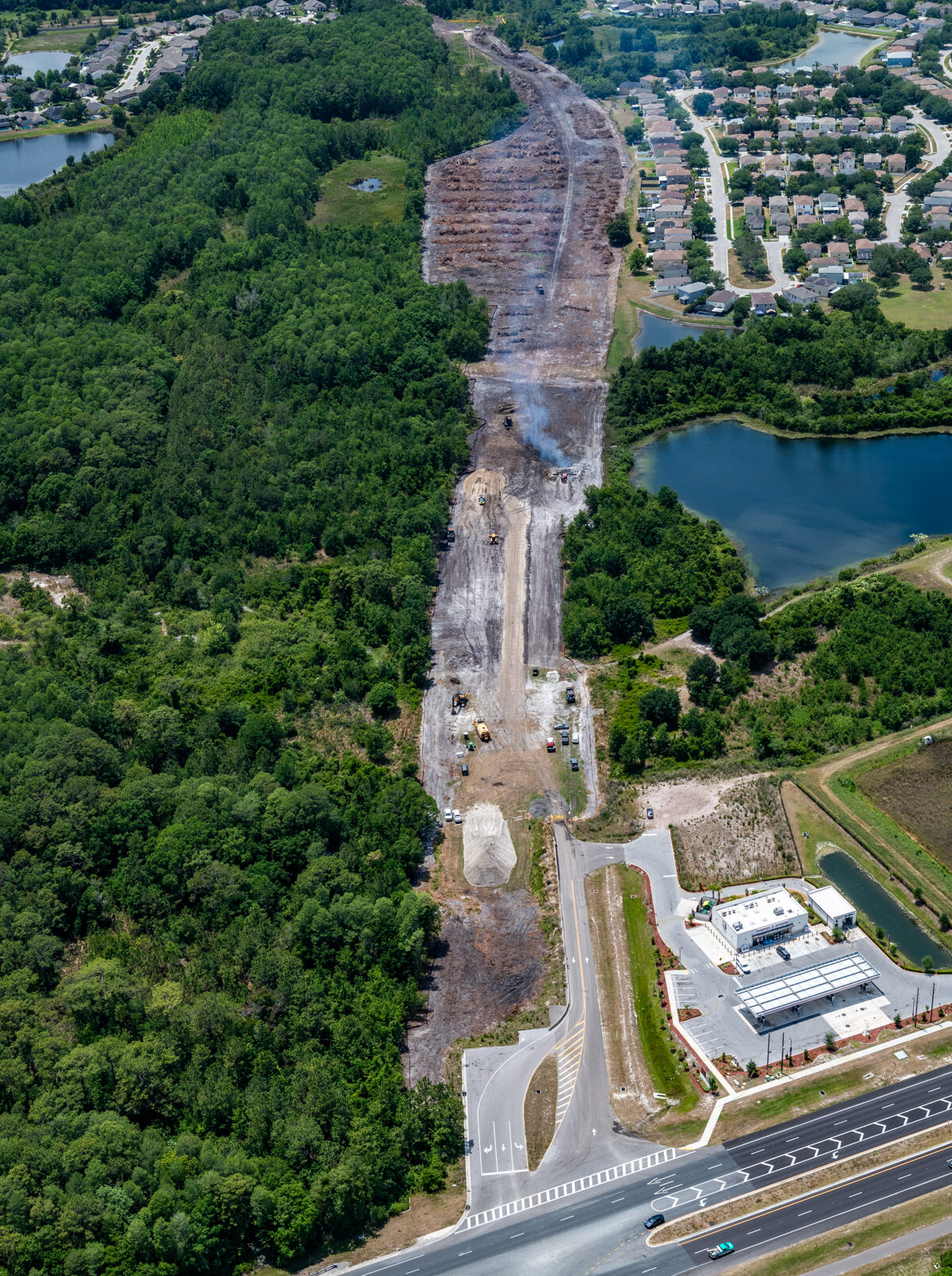 Aerial view of a road construction site through dense green forest adjacent to residential area