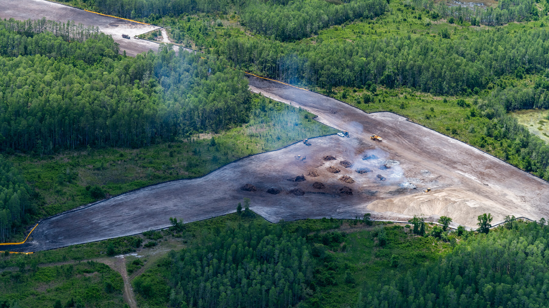 Aerial view of a forest clearing, construction site with vehicles and smoke