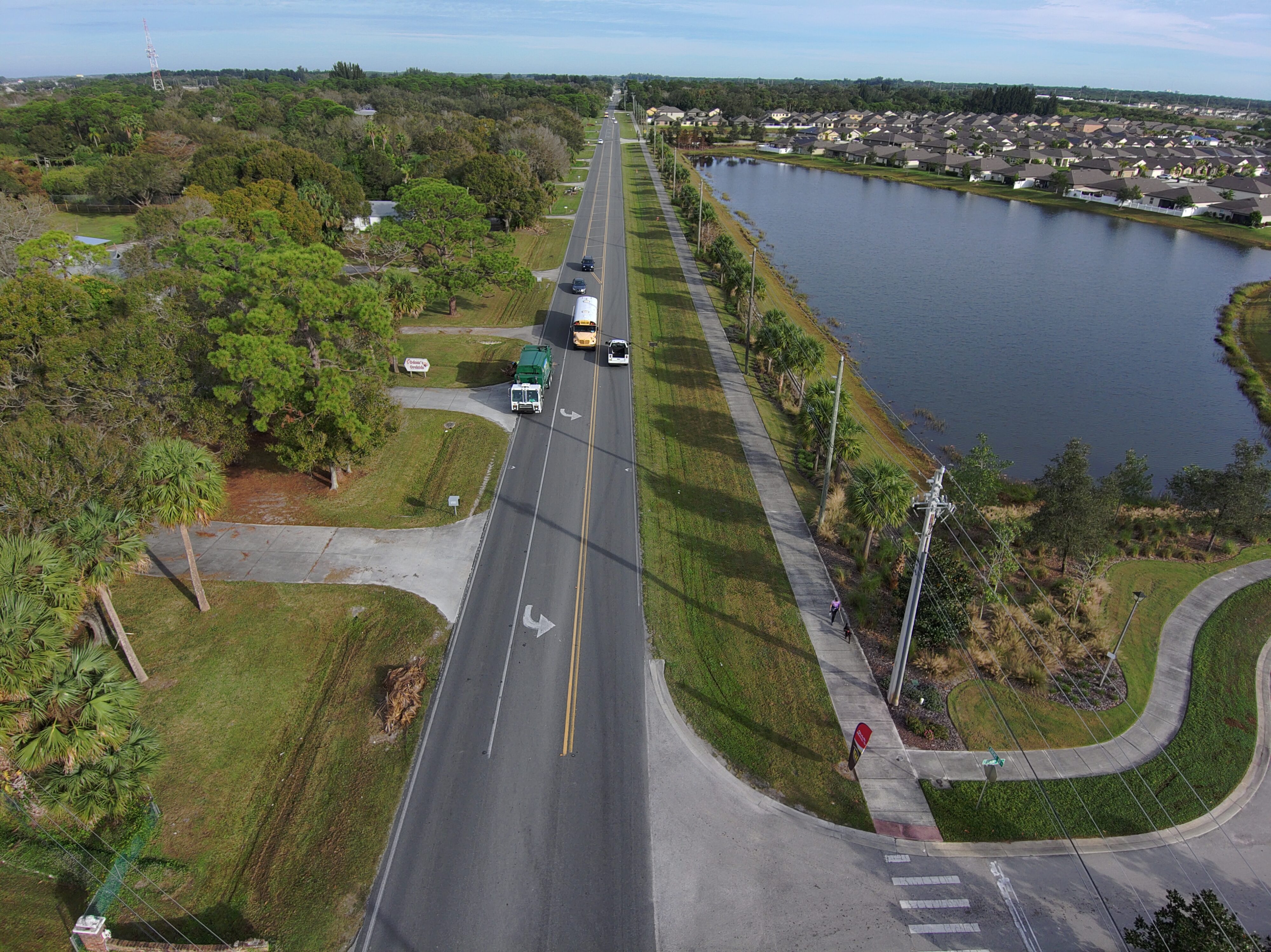 Aerial view of a long road flanked by trees, houses, and a lake