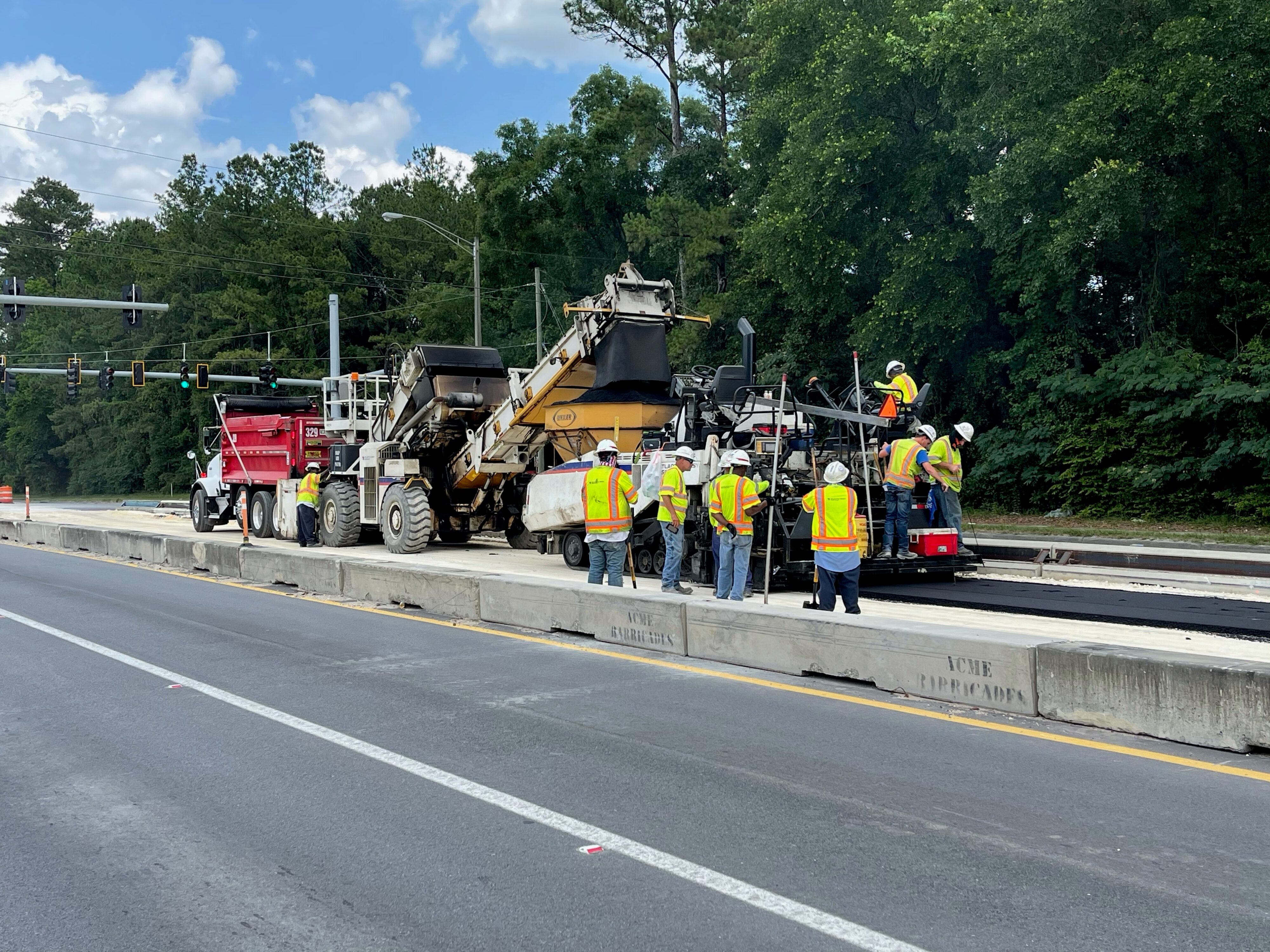Construction crew working on road paving near forest with heavy machinery