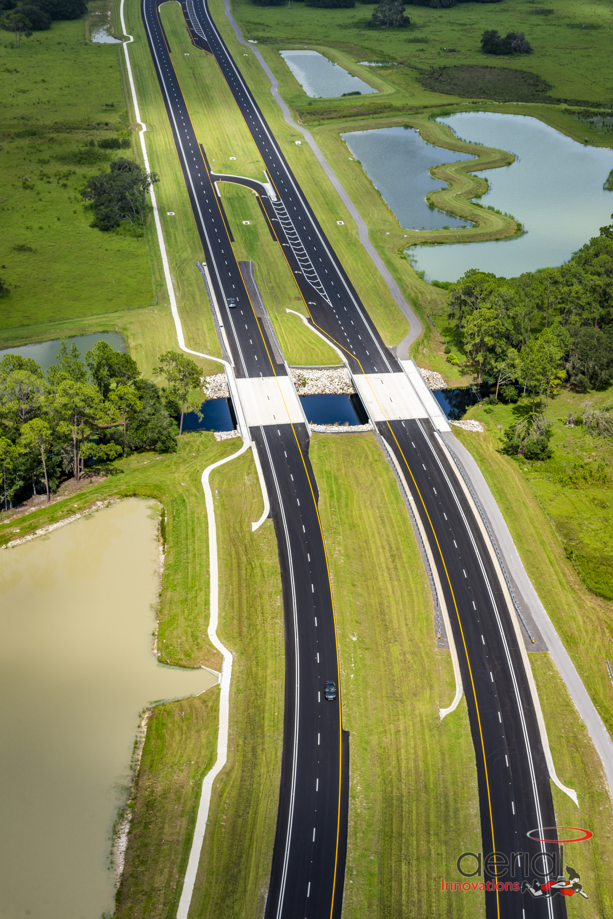 Aerial view of a divided highway with green fields and ponds on either side