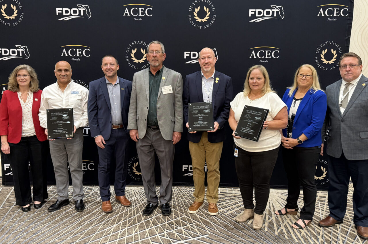 Eight people standing at an awards event; two holding plaques
