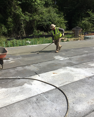 Worker in high-visibility vest smoothing concrete on a path with trees in background