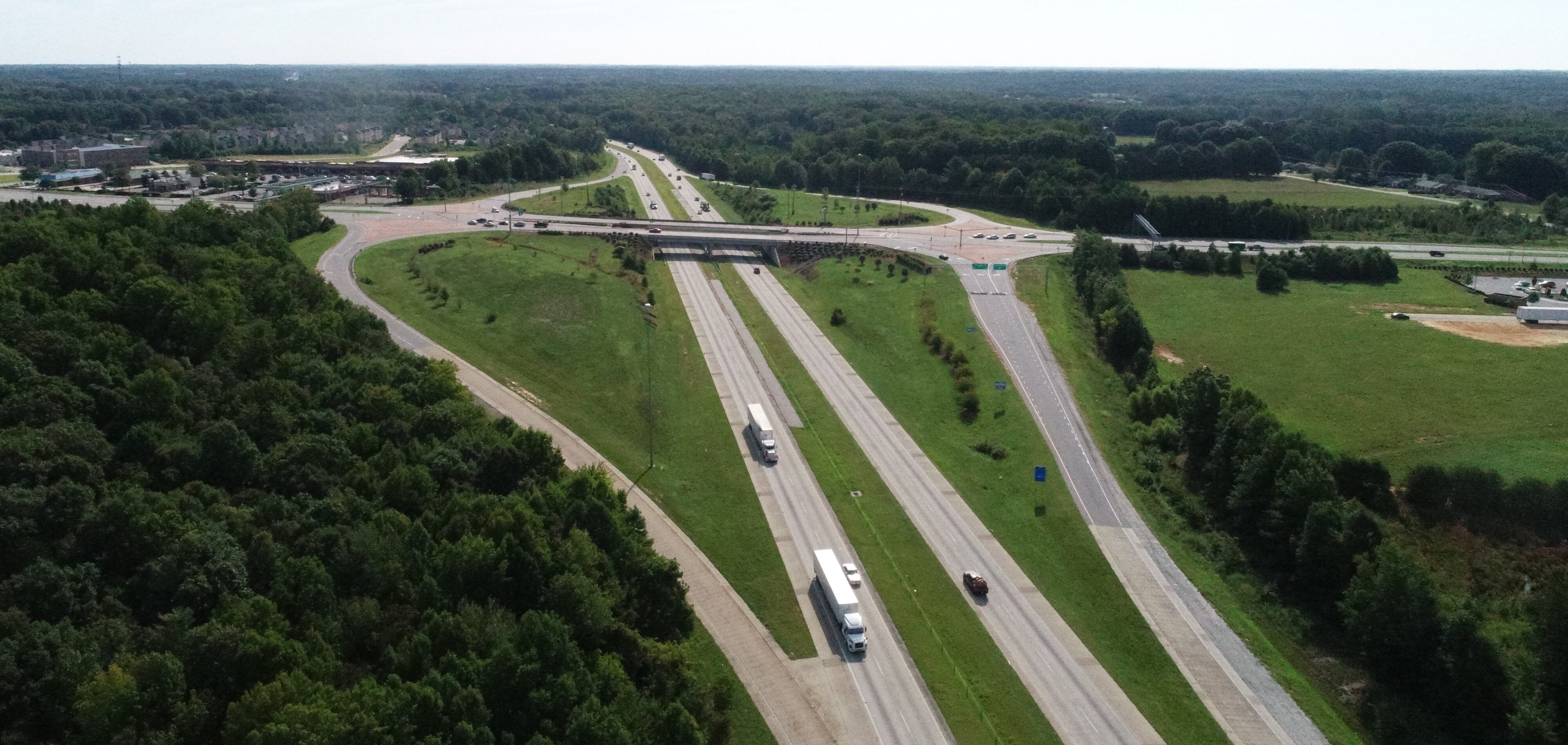 Aerial view of a highway interchange with trucks and cars, surrounded by greenery and trees
