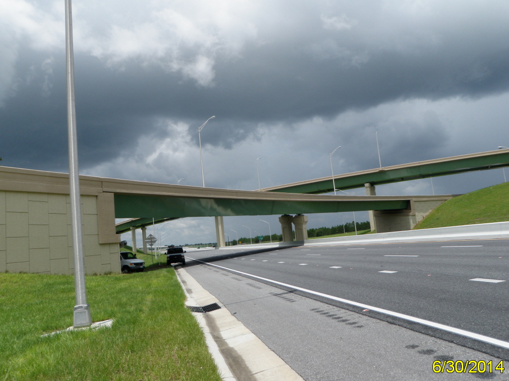 Overpass under stormy sky with cars parked below. Date: 6/30/2014