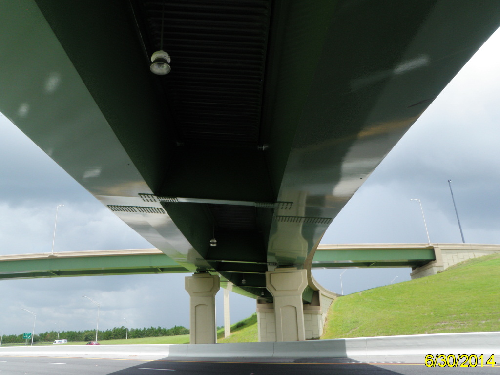 Underneath view of a green highway overpass against a cloudy sky