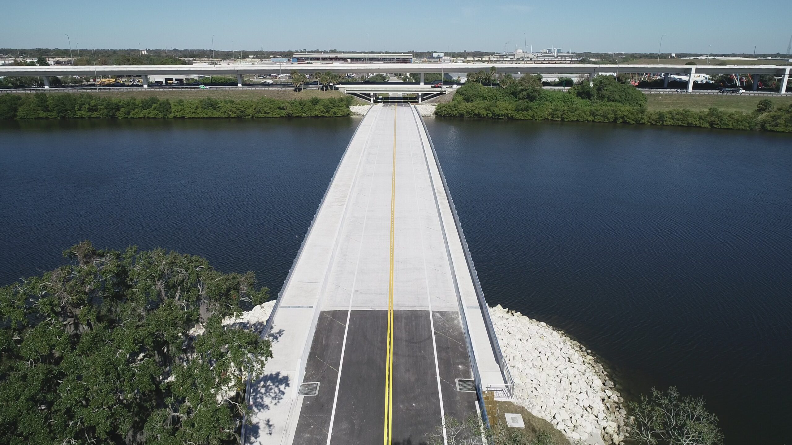 Aerial view of a long bridge spanning a wide river, surrounded by greenery and highways in the background