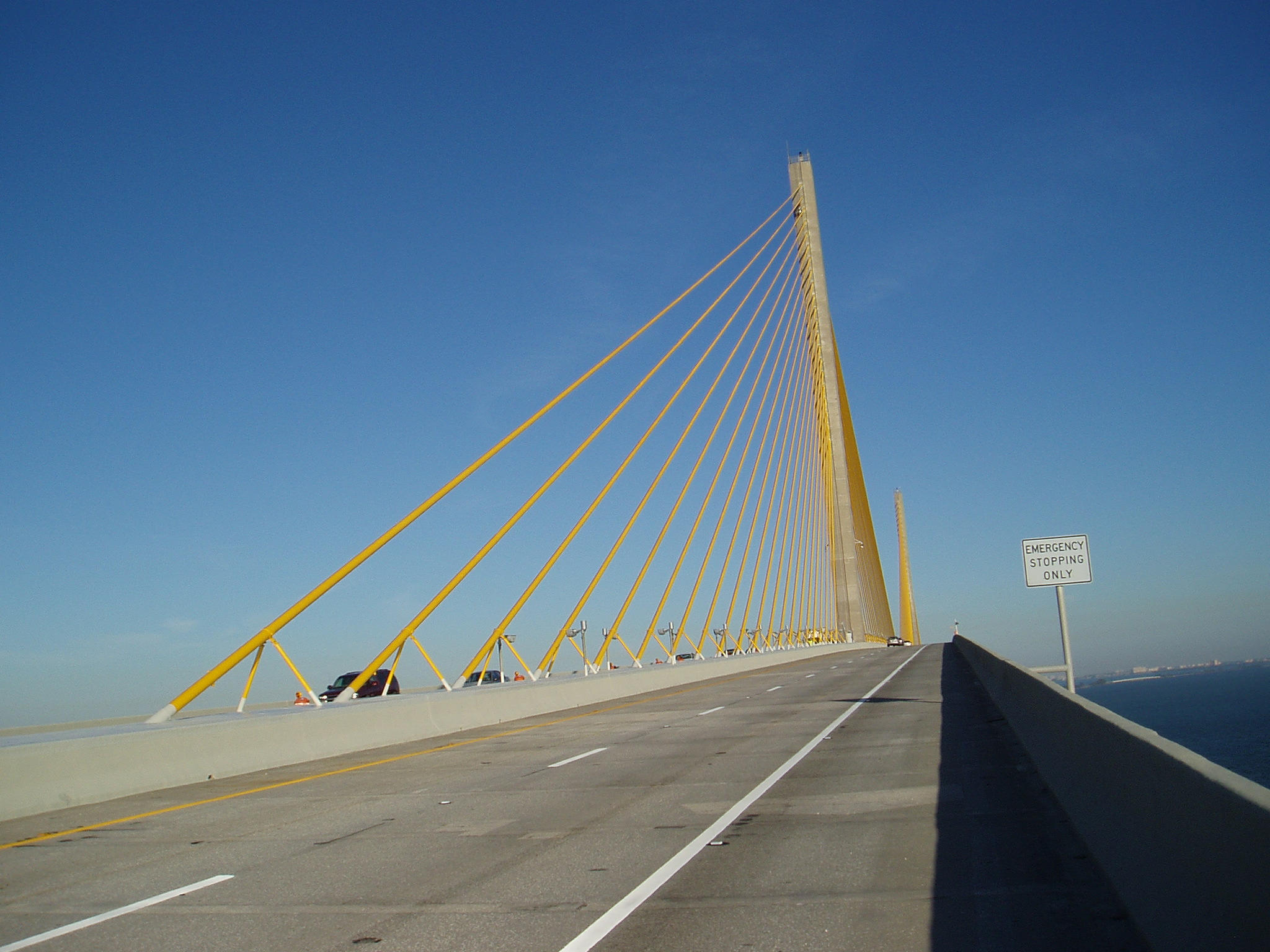Cabling-supported bridge with yellow cables under clear blue sky, sign reads "Emergency Stopping Only"