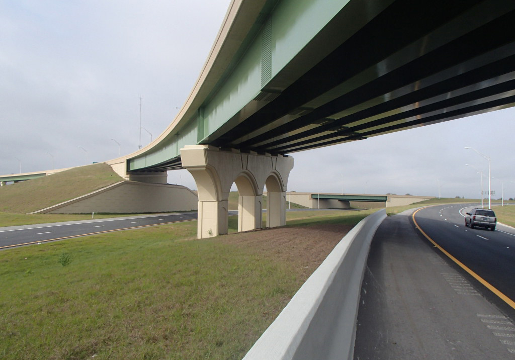 Elevated highway overpass with a car driving below, overcast sky
