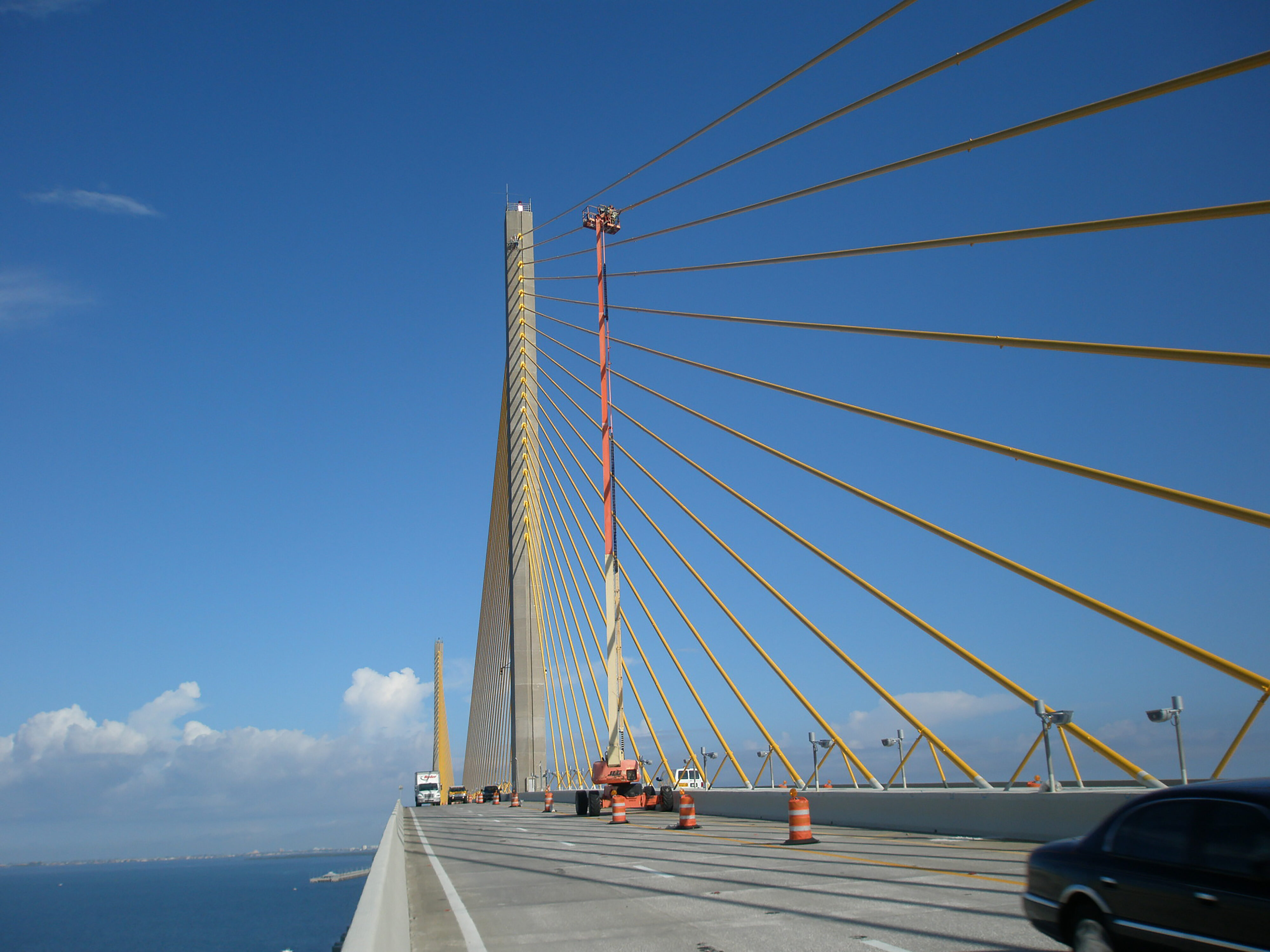 Suspension bridge with cables, clear sky, and traffic cones on road
