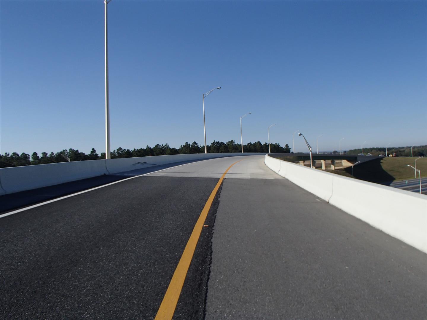 Empty highway curve under clear blue sky, surrounded by greenery