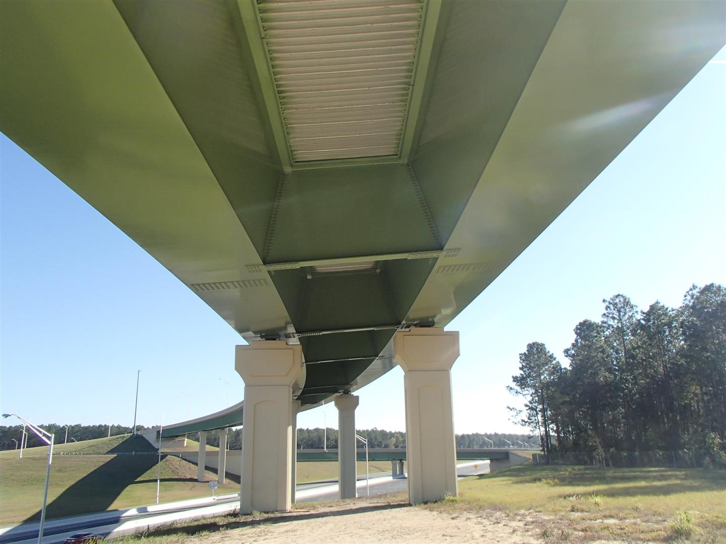 Underneath view of a green highway overpass with clear sky and trees