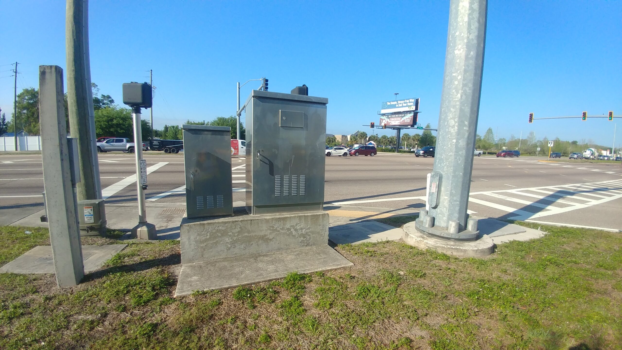 Metal utility boxes at a busy intersection with traffic lights and vehicles