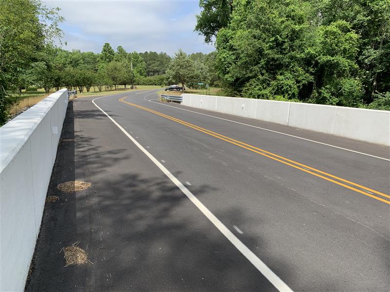 Curved two-lane road with white barriers, flanked by trees and greenery