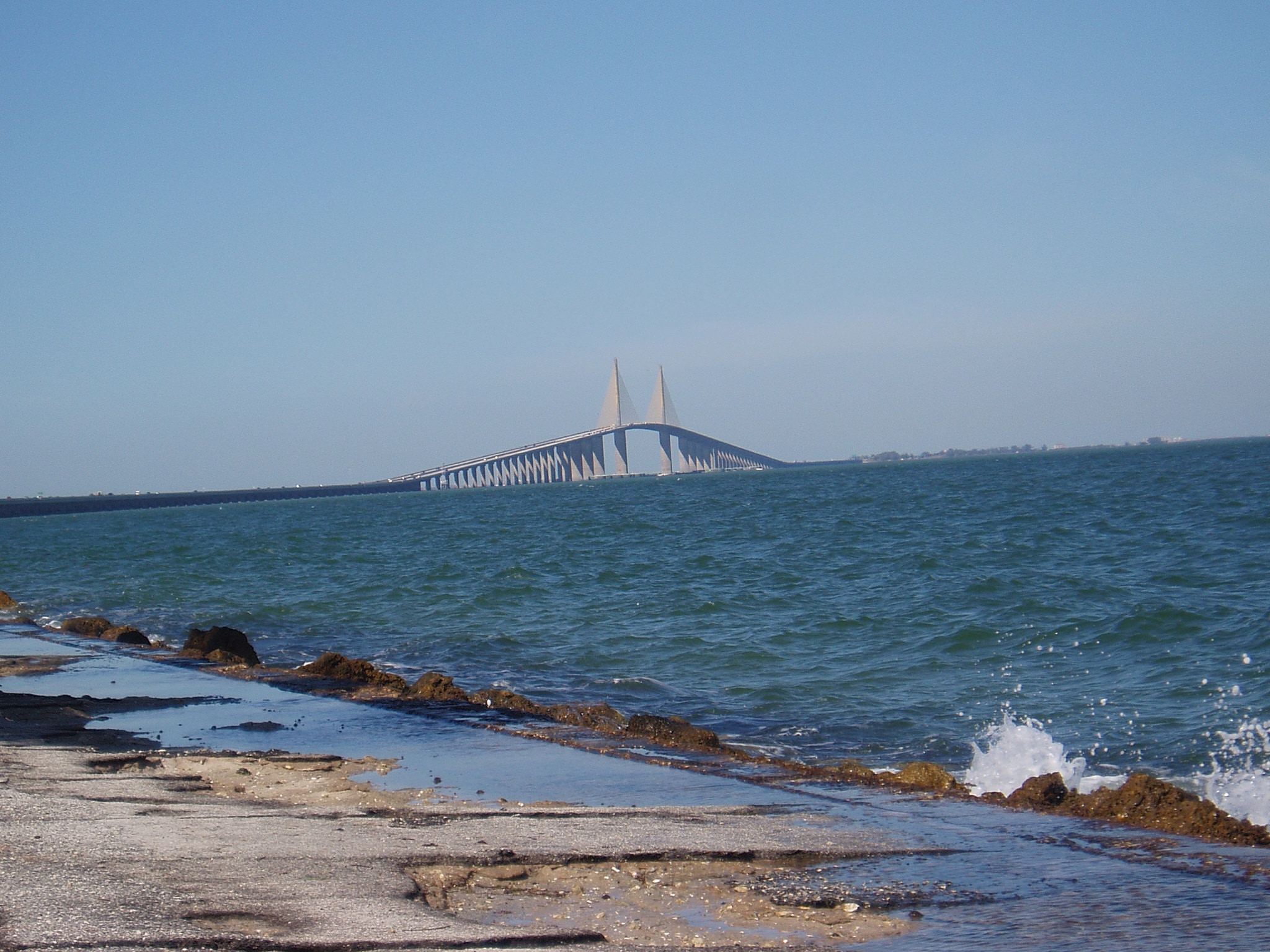 Skyway Bridge spans blue ocean beneath clear sky, rocky shoreline