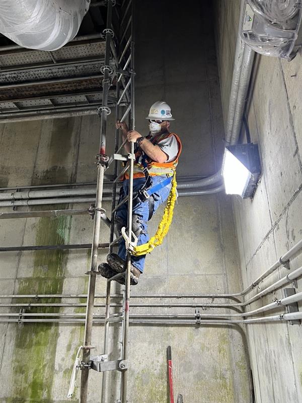 Construction worker climbing scaffolding in industrial setting wearing safety gear