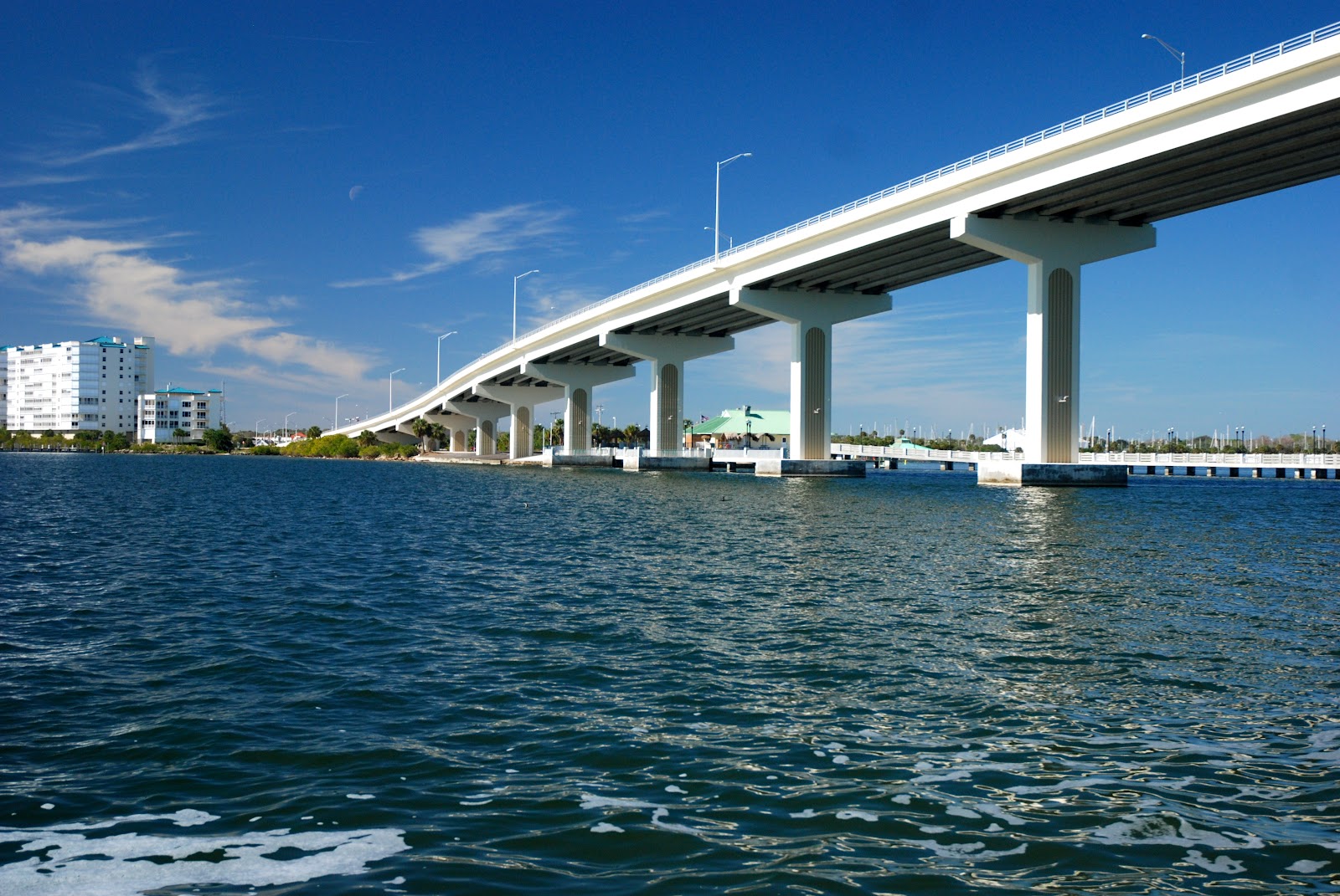 Curved white bridge crossing over blue water under a clear sky