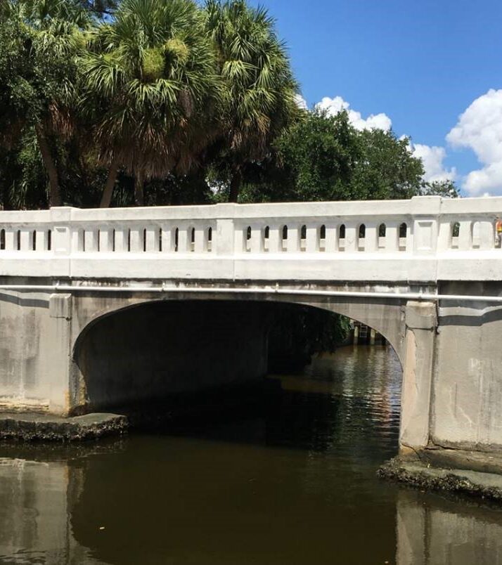 White arched bridge over a calm waterway with surrounding trees