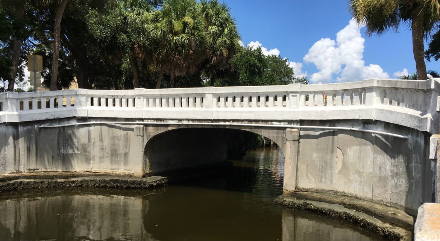 White arched bridge over a calm waterway with surrounding trees